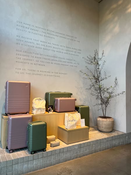 The ad features a collection of suitcases and bags from a travel brand, displayed in a minimalist setting with a wall qu