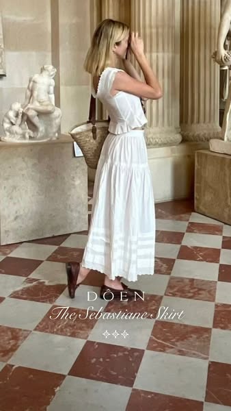 This ad features a woman wearing a white skirt and top from the brand DÔEN. She is standing in what appears to be a muse