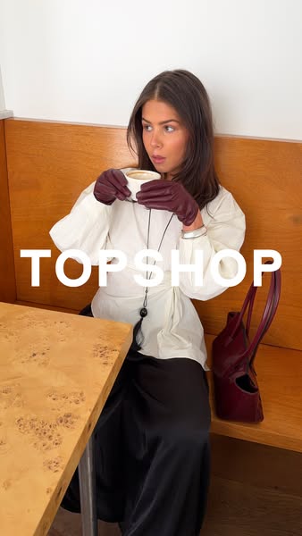 A stylish image ad featuring a woman at a cafe table wearing gloves and holding a cup. The brand name, Topshop, is promi