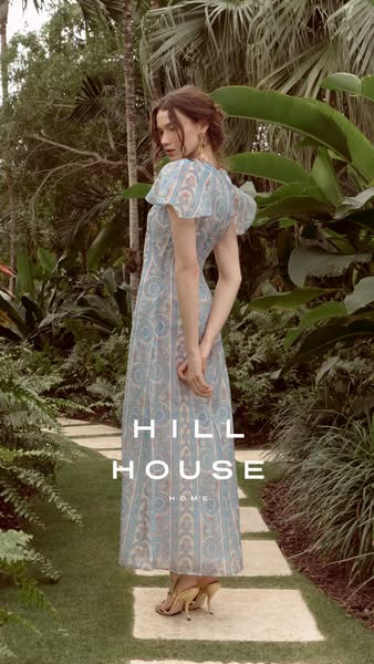 This ad for Hill House Home features a woman standing outside in a garden setting wearing a full-length light blue patte
