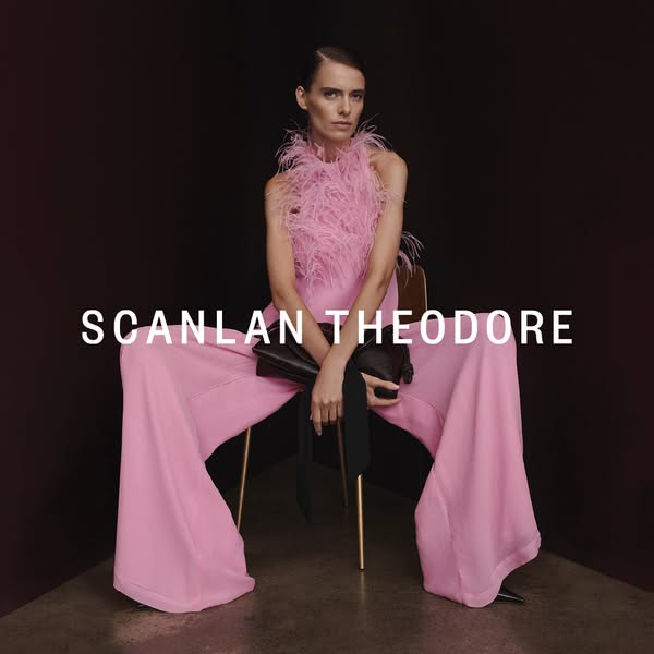 This ad features a full shot of a model wearing a pink Scanlan Theodore wide-legged halter jumpsuit with feathered detai