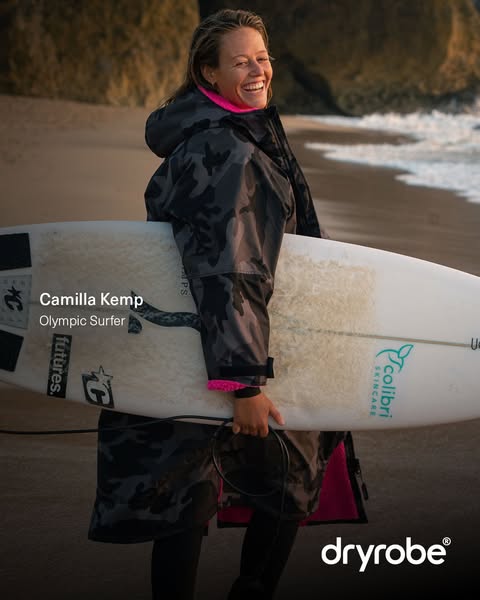 This image ad features Camilla Kemp, an Olympic Surfer, wearing a Dryrobe changing robe on a beach. The photo captures a