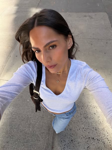 A selfie-style photo of a woman wearing a long-sleeve top and jeans.