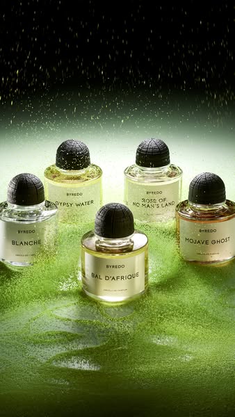 This ad promotes Byredo perfumes by showcasing five different scents in glass bottles with black caps arranged on a gree