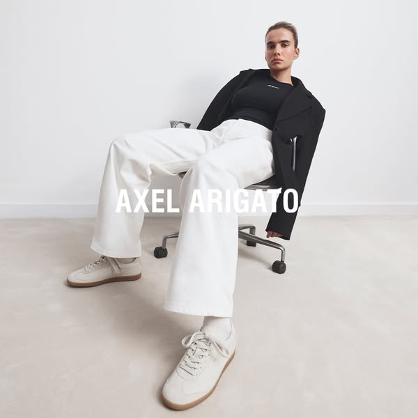 An ad showcasing the brand Axel Arigato, featuring a woman sitting in a chair, wearing the brand's apparel and shoes
