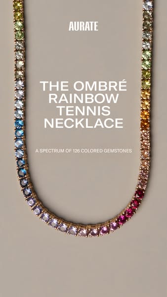 Image ad showcasing a gold Aurate tennis necklace with gemstones arranged in an ombre rainbow gradient.