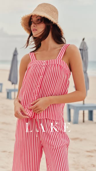 A woman on a beach wears a matching red and white striped tank top and pants from LAKE. The neutral colors of the beach 