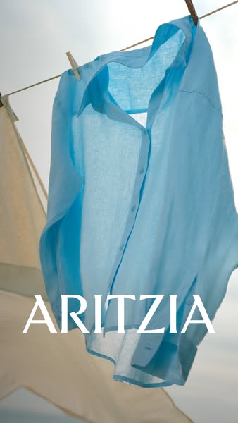 This Aritzia image ad features a blue button-down shirt hanging on a clothesline against a sky background. The brand nam