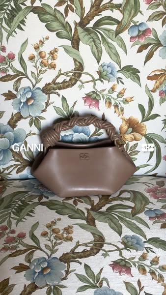 This image ad showcases a GANNI leather handbag. The bag is placed against a floral backdrop. The ad has a simplistic st