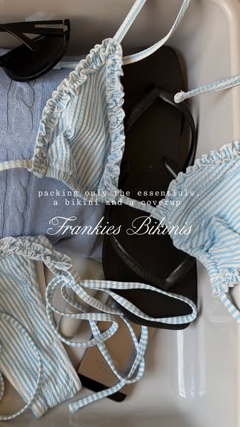 This image shows a Frankies Bikinis bikini top and bottoms, black flip-flops, and a light blue knit sweater being packed
