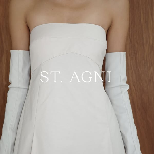 A brand ad for St. Agni apparel. The ad features a woman wearing a white dress and long white gloves.