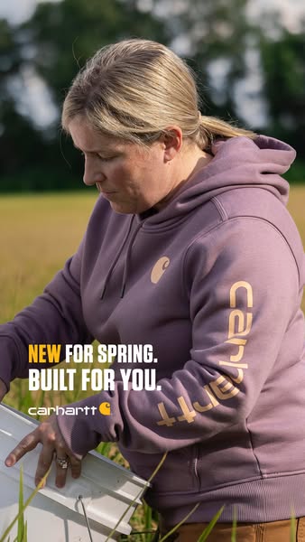 An ad for Carhartt, showcasing a woman in a Carhartt hoodie outdoors, implying it's built for spring.