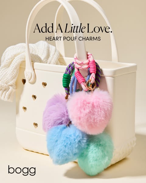This ad showcases a Bogg bag, a durable and waterproof tote, accessorized with heart-shaped pouf charms attached to the 