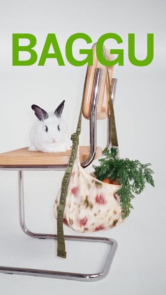 This image ad features a Baggu bag hung on a modern metal chair with a plush toy rabbit placed on the seat. The shot is 
