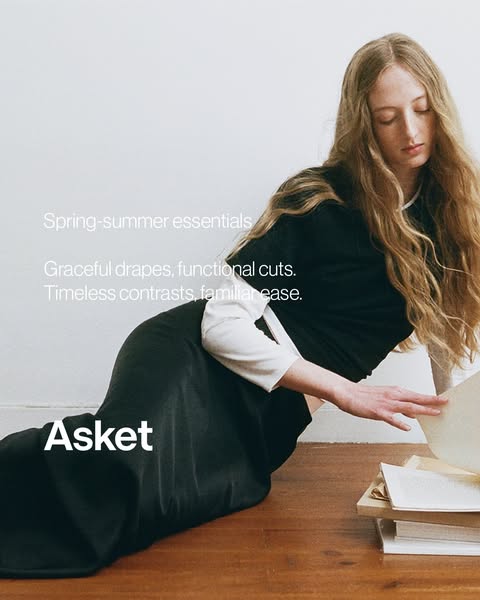An image ad for Asket apparel features a woman in a long black skirt and a black tee shirt over a white long-sleeved shi