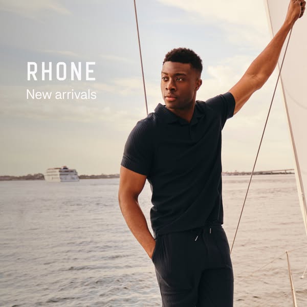 An image ad for Rhone, a men's clothing brand, featuring new arrivals. The ad shows a man on a boat, wearing a dark-