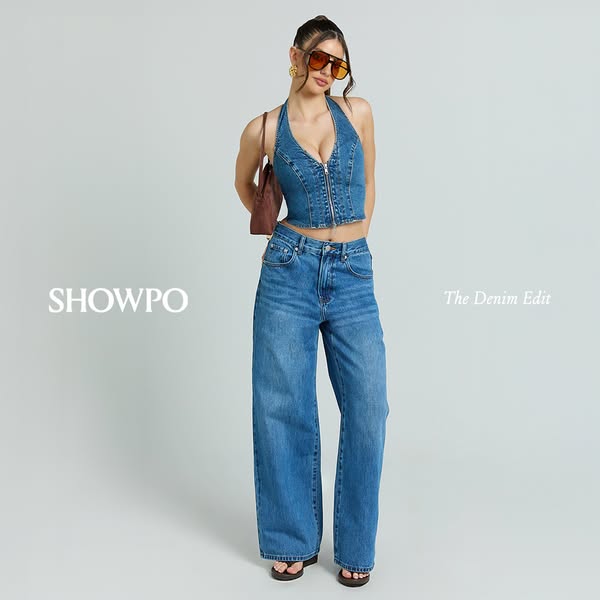 This ad showcases a woman wearing a denim halter top and wide-leg jeans from Showpo's 'The Denim Edit' colle