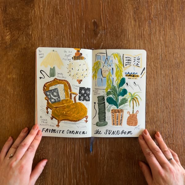 The ad features a colorful, hand-drawn illustration from an open sketchbook sitting on a wooden table. The illustration 