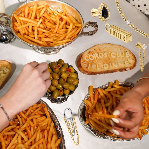 This ad promotes jewelry by displaying various jewelry pieces around a table with french fries, olives and bread.