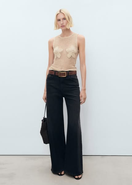 This ad showcases a woman wearing a tan knitted top, dark wide-leg jeans, and sandals. She is holding a bag, and the bac