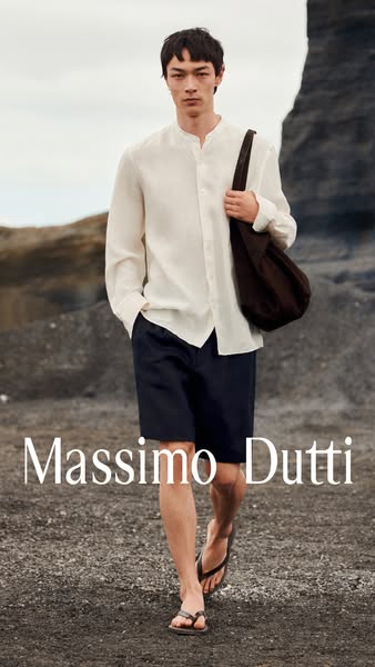An outdoor lifestyle shot of a male model wearing Massimo Dutti products, including a linen shirt, navy shorts, sandals,