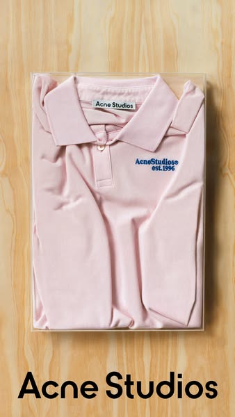 This is an image ad showcasing a pink Acne Studios polo shirt packaged in a clear rectangular case. The image features a