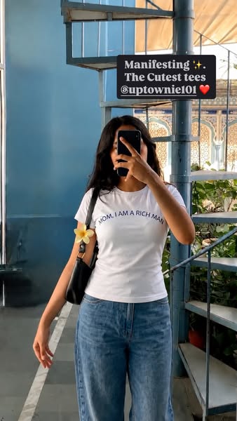 An image ad for Uptownie Girl tees featuring a woman in a 'Mom, I am a Rich Man' t-shirt taking a selfie in fron