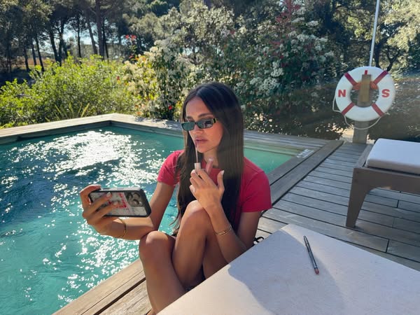 The image ad shows a woman sitting outside near a pool, applying makeup while on a video call with someone on her phone.