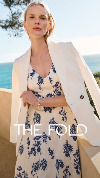 An ad featuring The Fold brand. It showcases an ivory-colored dress with navy floral prints and is paired with a white b