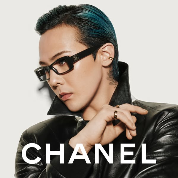 This Chanel ad features a person with blue hair wearing Chanel glasses, rings, and a leather jacket against a light back