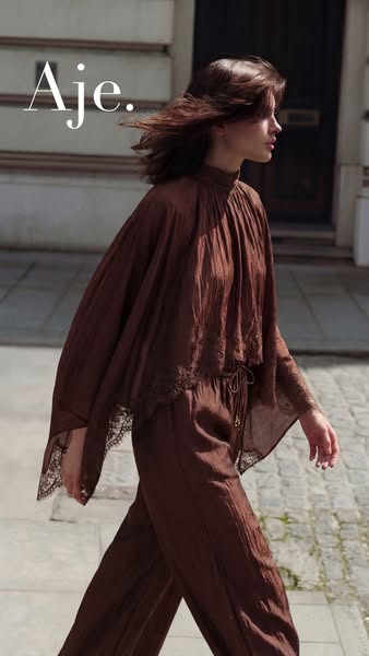 An advertisement for Aje. featuring a woman walking down a street wearing a matching top and pants outfit.