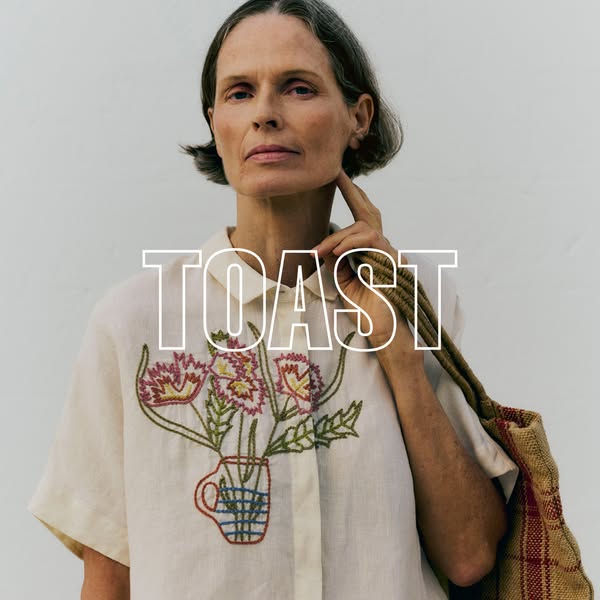 This image ad features a woman wearing a Toast brand blouse with an embroidered flower design. The brand name is display