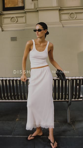 A waist-up shot of a female model wearing a tank top and skirt from Dissh. The brand's name is featured, along with 