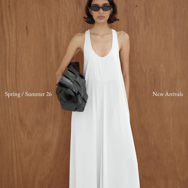 This image ad showcases a woman wearing a white dress and holding a black woven bag from the brand's new Spring/Summ