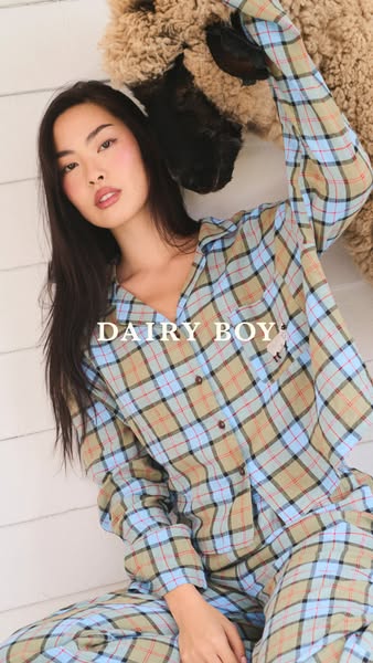 A woman relaxes in a set of plaid pajamas alongside a large stuffed animal. The ad promotes the Dairy Boy brand.