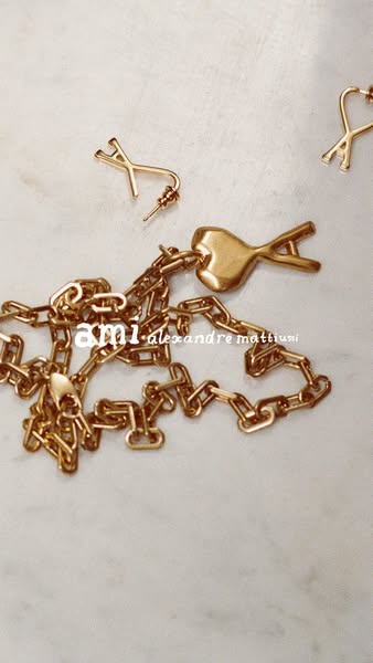 This ad showcases Ami Alexandre Mattiussi jewelry, including a necklace and earrings, against a neutral background.