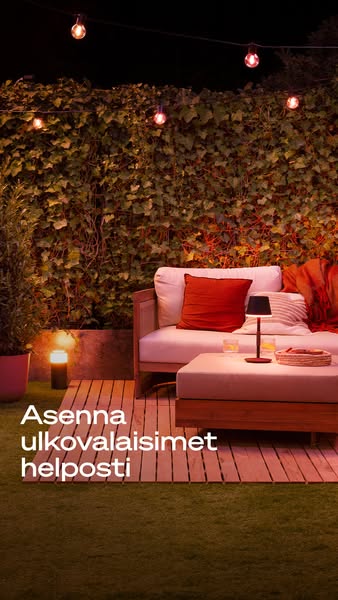 An outdoor scene featuring a backyard set-up with a wooden sofa and ottoman, an outdoor lamp, string lights and a call t