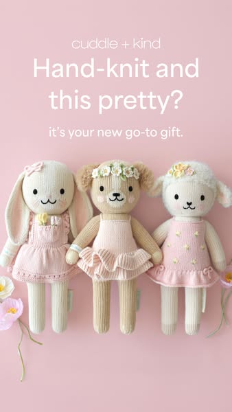 This ad features three cuddle + kind dolls standing side-by-side. The dolls are hand-knit and dressed in pink dresses, m