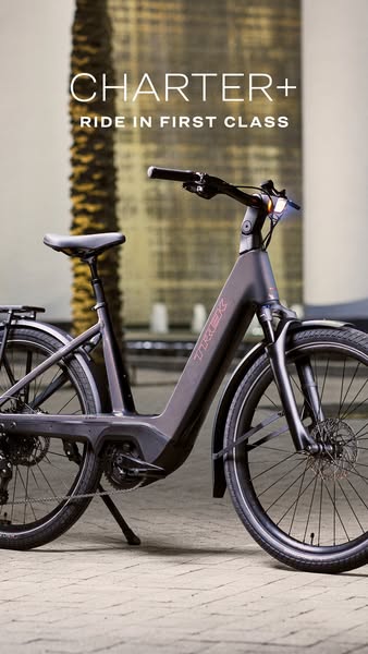 This ad features a dark grey Trek e-bike in an urban setting with a focus on the brand's Charter+ model and position