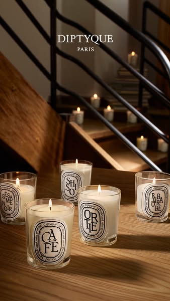 An overhead product shot featuring Diptyque candles. The shot is staged in a way that implies an elegant and cozy settin