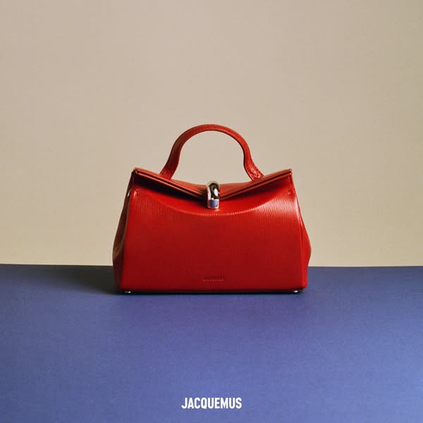 This image ad features a red handbag by Jacquemus, presented against a two-tone backdrop. The focus is on the bag's 