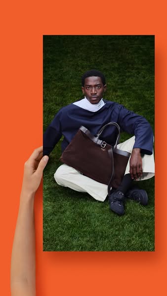 This ad features an image of a person sitting on the grass and holding a dark brown tote bag. A hand is holding the imag