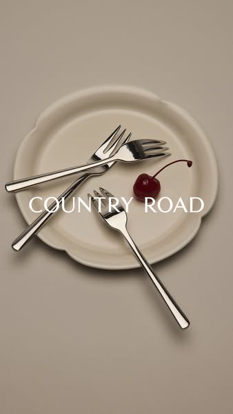 This image ad for Country Road features a minimalist flat lay of three dessert forks and a cherry on a plate, set agains
