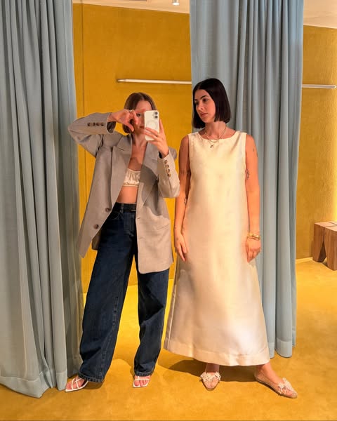 This ad features two women in a store or dressing room, one wearing a dress and one taking a selfie. It showcases the dr