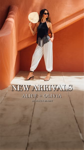 This ad for Alice + Olivia features a woman wearing a black halter top with silver tassels and white pants. She is holdi