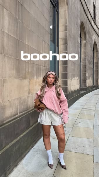 This image ad features a woman modeling an outfit from Boohoo. She is wearing a pink sweater, white shorts, white socks,