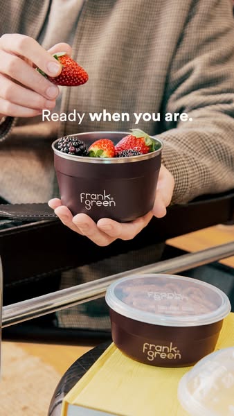 This ad shows a person adding a strawberry to a Frank Green container filled with berries. There is another Frank Green 