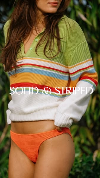 An eye-level studio shot of a woman wearing a sweater and bikini bottoms by Solid & Striped. The shot focuses on the
