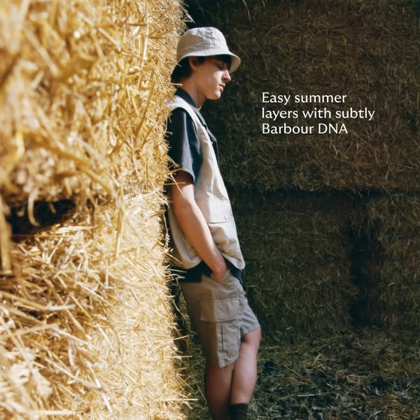 This image ad promotes Barbour clothing for summer by featuring a man in layered outfits standing against stacked hay ba