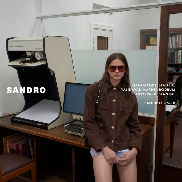 This ad for Sandro showcases a model wearing a brown jacket with gold buttons and striped shorts. The ad promotes Sandro